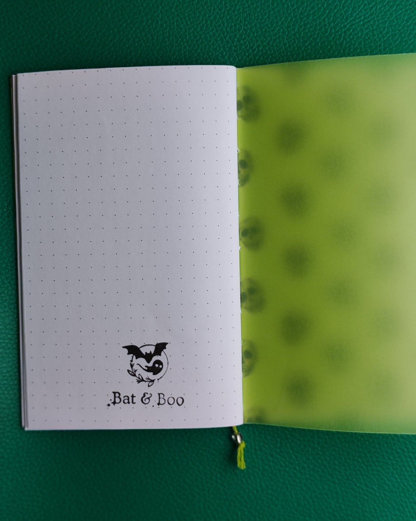 Open notebook with dotted pages and green interior on a green background, showing business logo stamped on final page