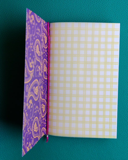 Open notebook with purple paisley patterned cover and yellow checkered page on a teal background