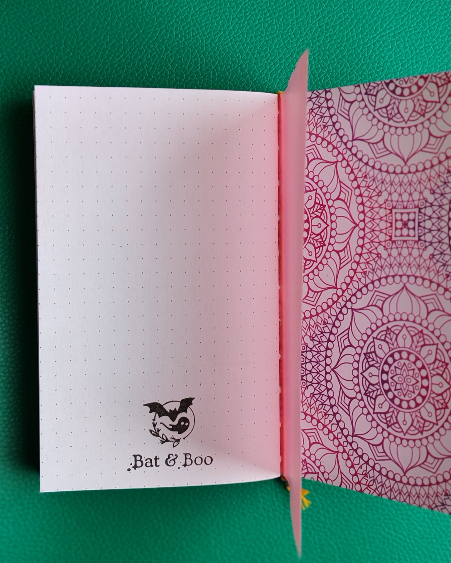 Open notebook with one page showing a white interior with logo and the other with a red mandala design on a green background.