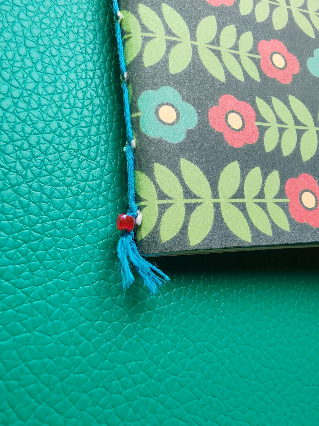 Floral-patterned notebook with bead & tassel on a teal background