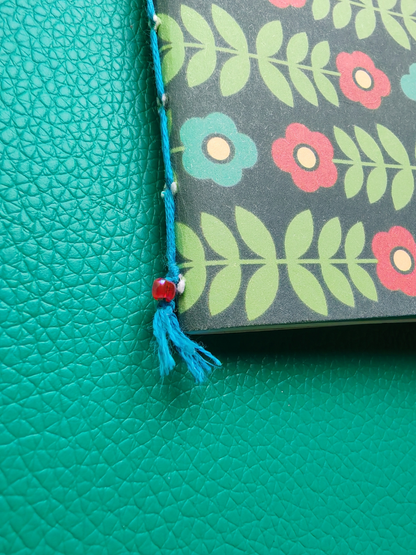 Floral-patterned notebook with bead & tassel on a teal background