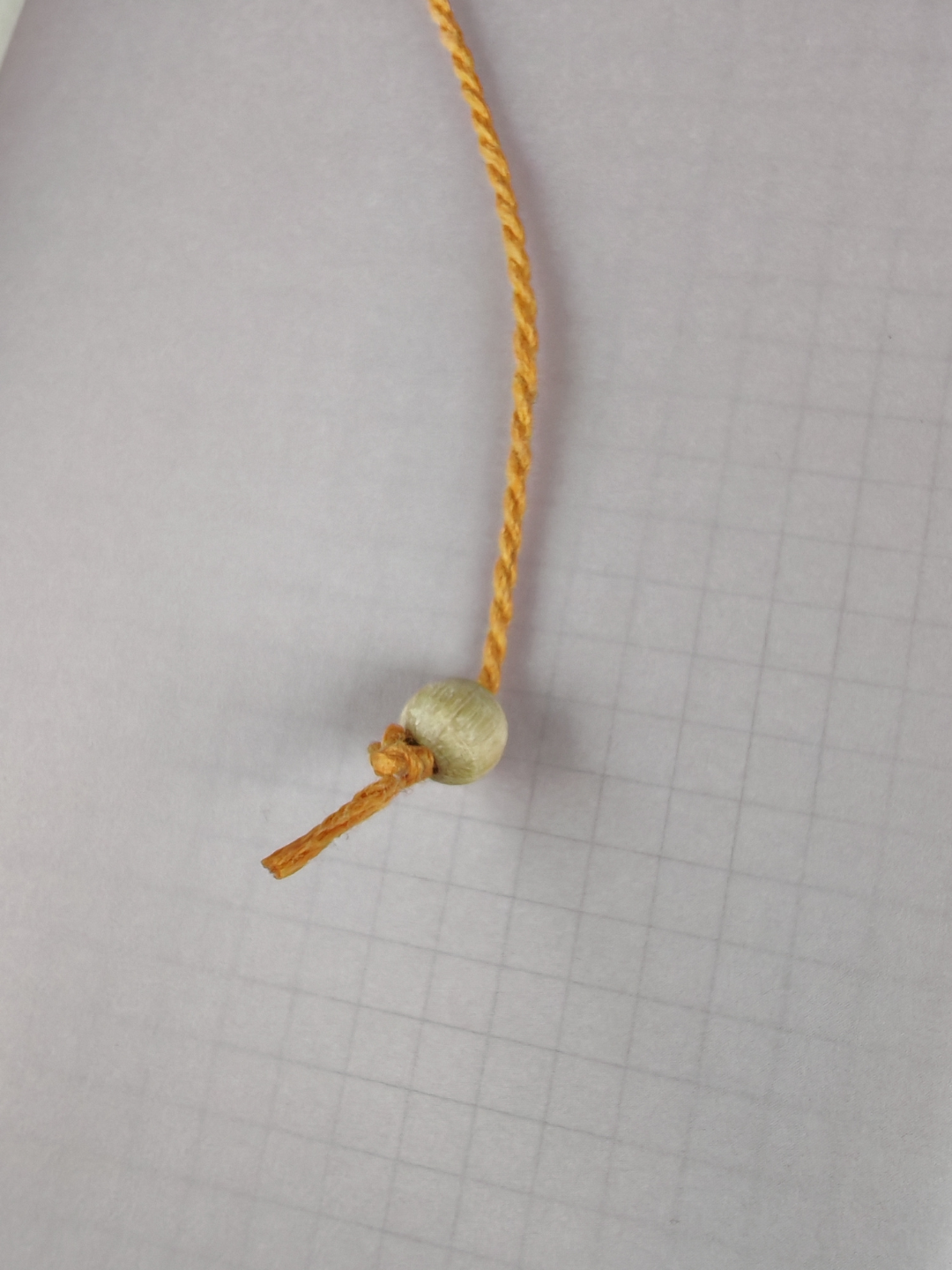 Yellow cord with a wooden bead on a grid paper background