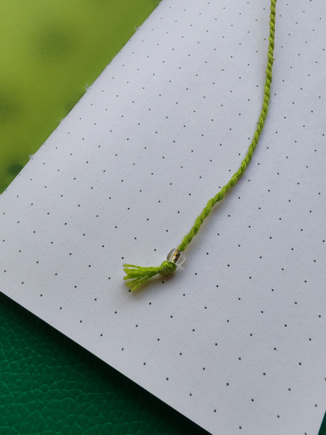 Close-up of a green thread bookmark with a glass bead
