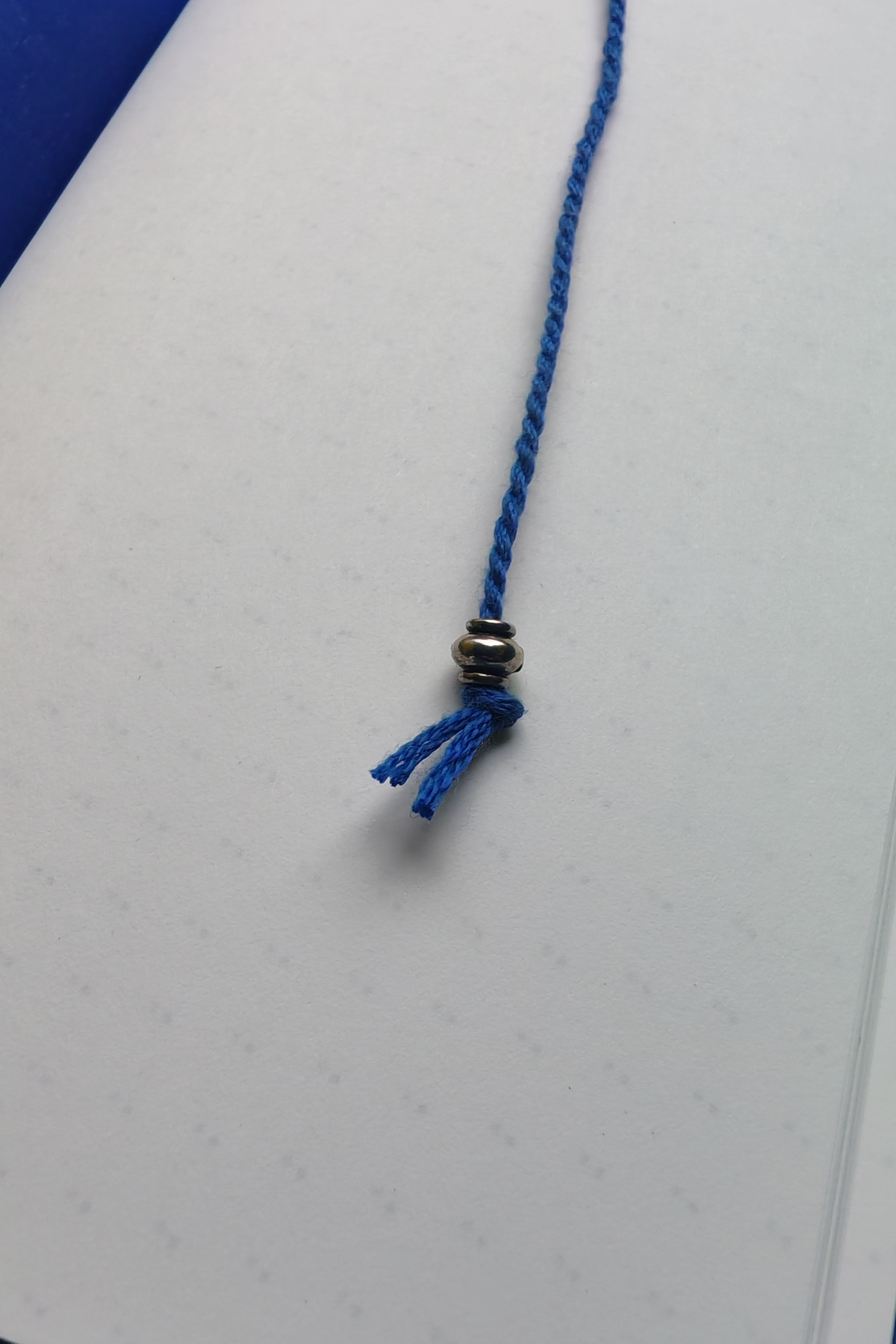 Blue braided cord with a metal bead on a white background