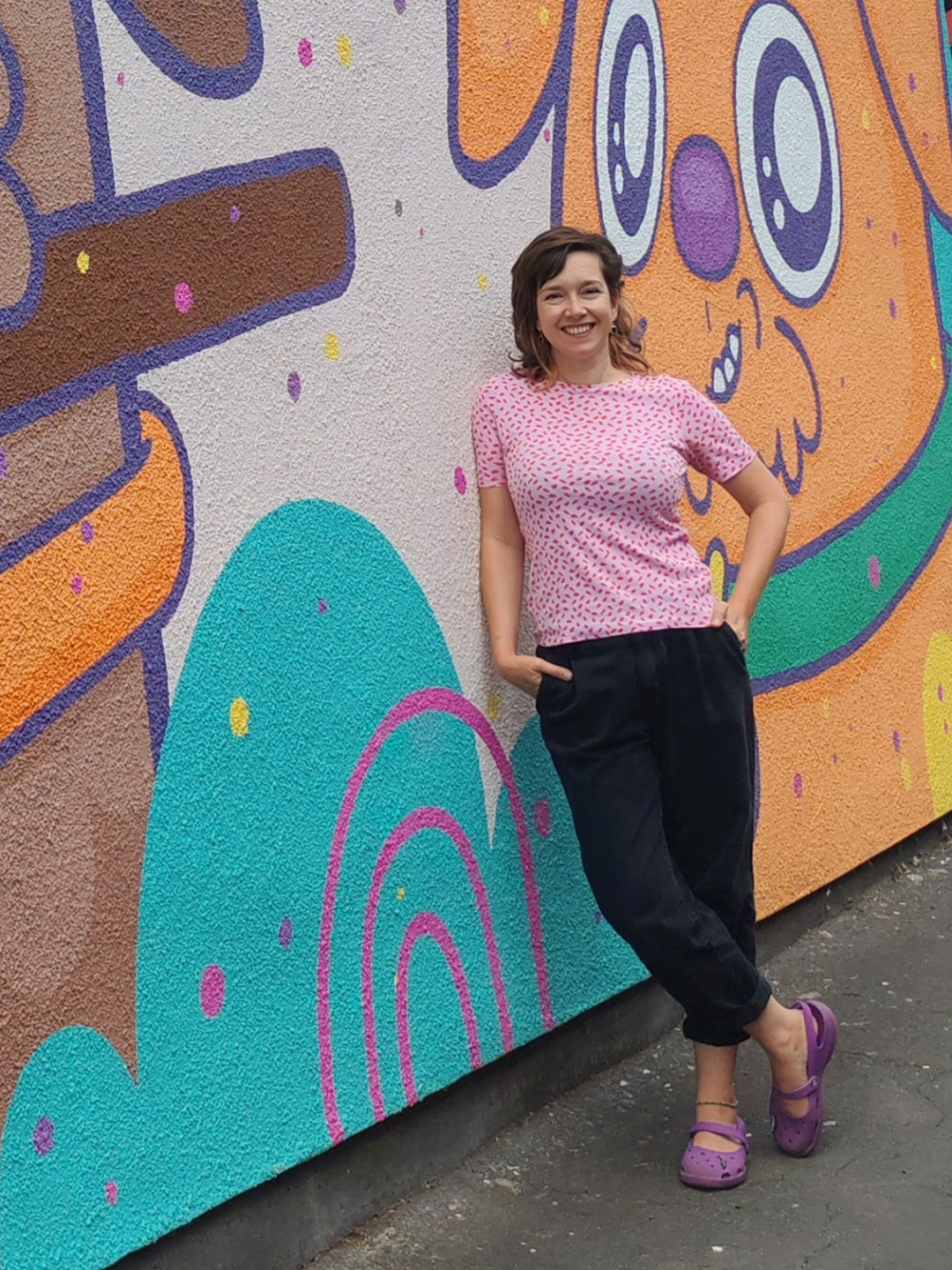 Woman in a pink shirt standing in front of a colorful mural