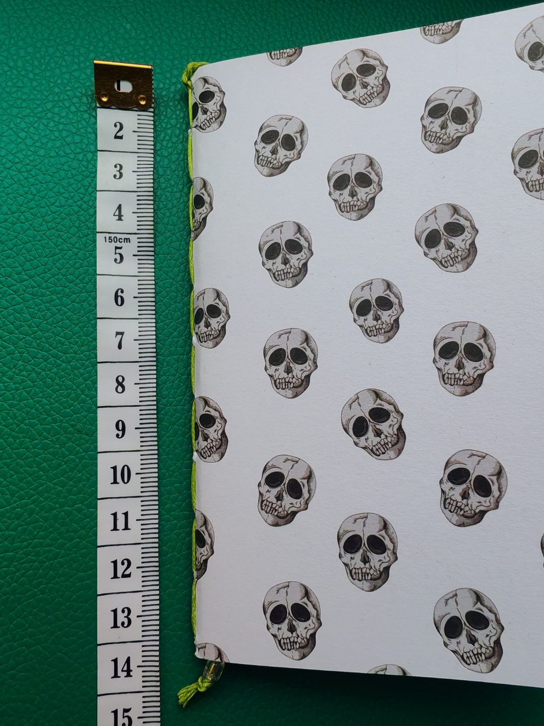 Notebook with skull pattern on a green background next to measuring tape