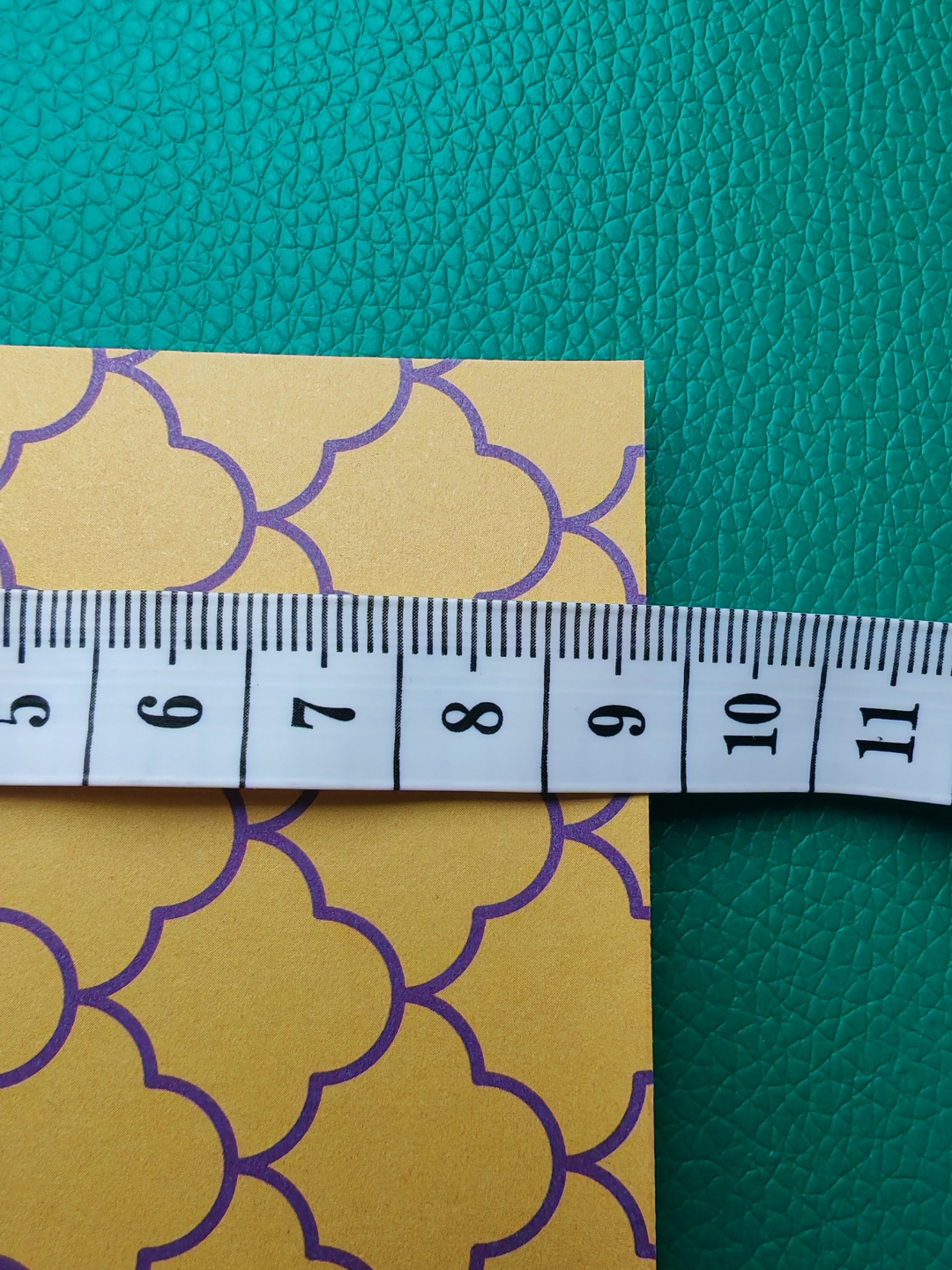 Yellow paper with purple patterns and a measuring tape on a green textured background