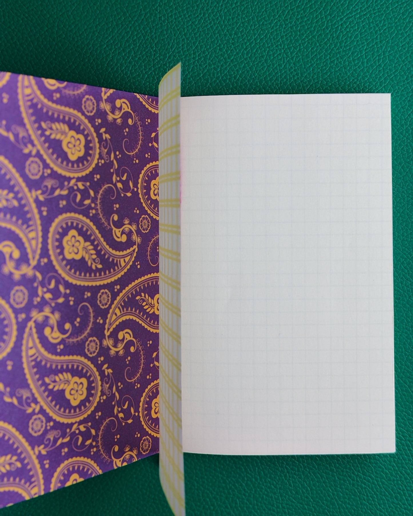 Open notebook displaying a purple paisley patterned inner cover, the grid patterned vellum inner page and a plain white first page of iroful paper