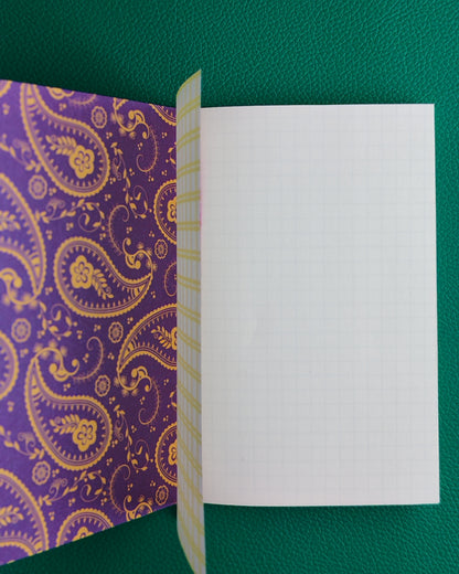 Open notebook displaying a purple paisley patterned inner cover, the grid patterned vellum inner page and a plain white first page of iroful paper