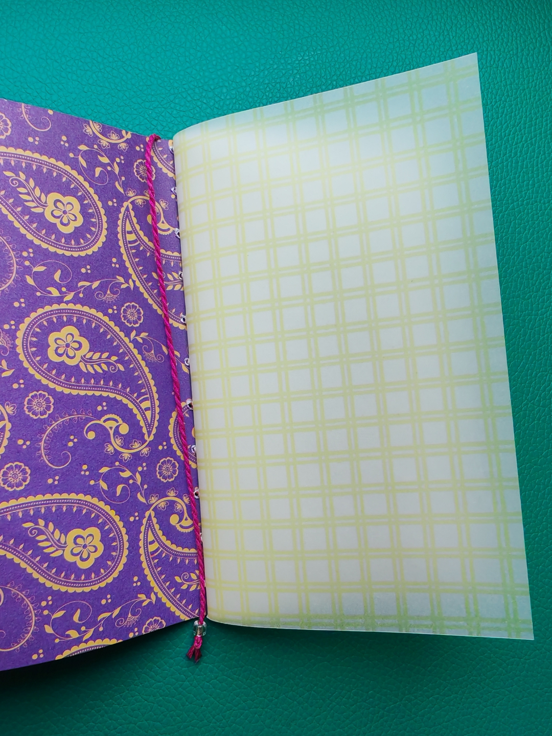 Open notebook with purple paisley design on one page and yellow checkered pattern on the other, on a green background.