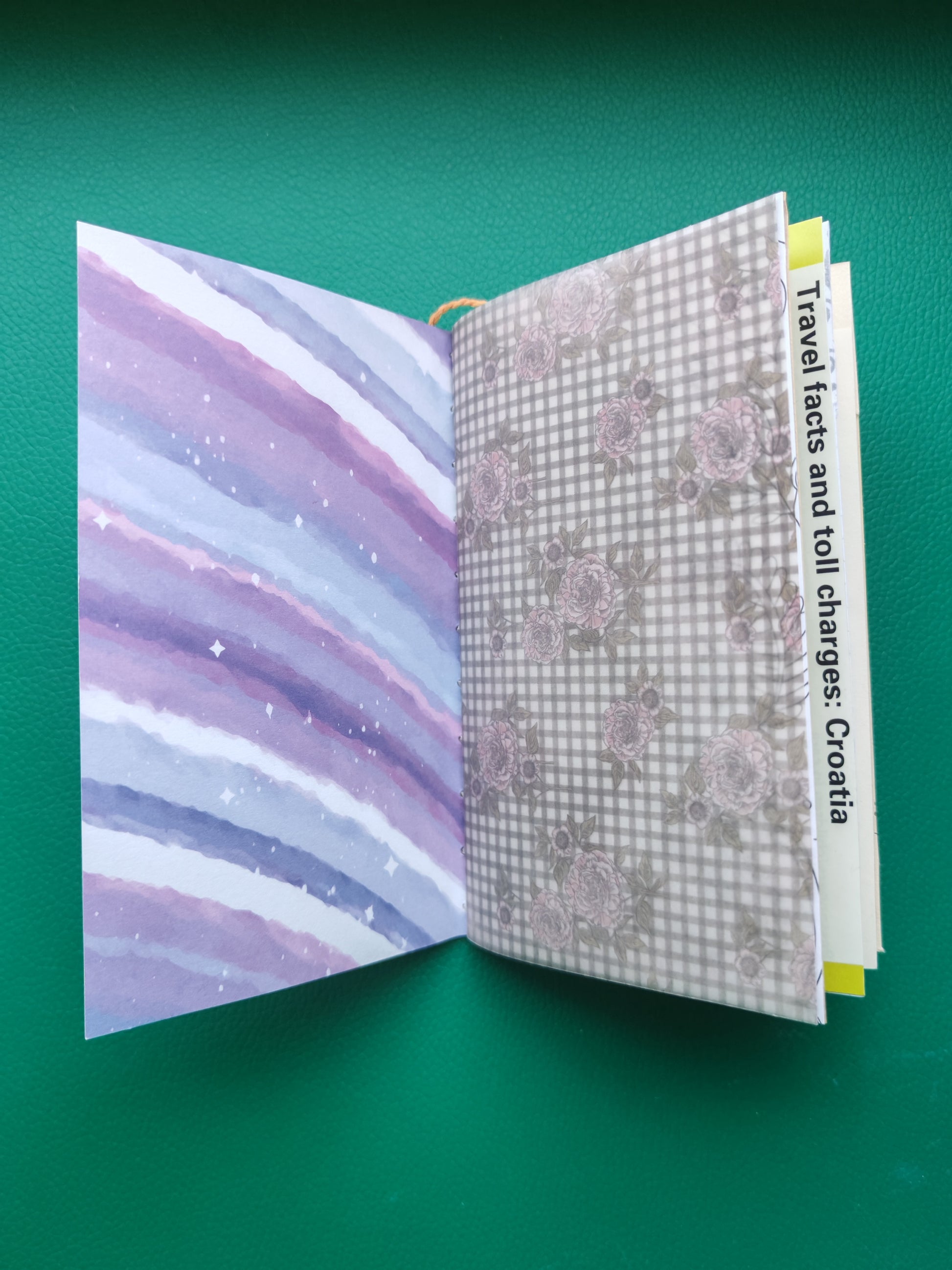 Open notebook with purple and white abstract design on one page and floral pattern on the other, on a green background.
