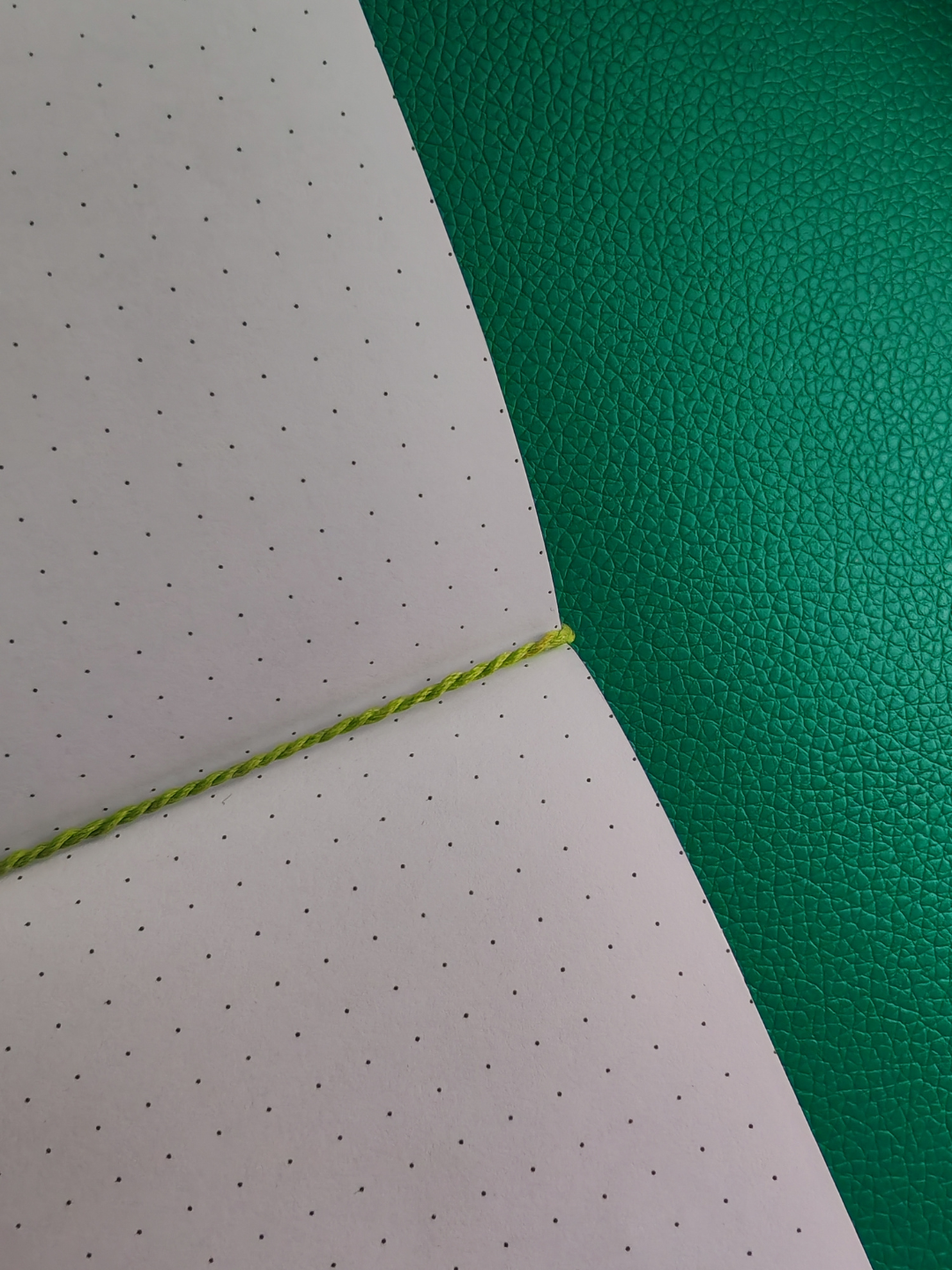 Corner of a notebook with green thread and green textured surface