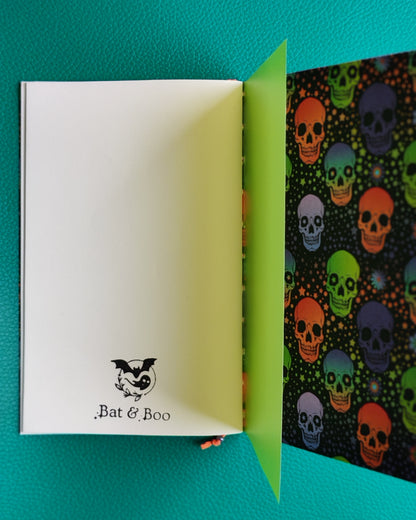 Open notebook with white page with stamped bat & boo logo and colorful skull pattern on green background