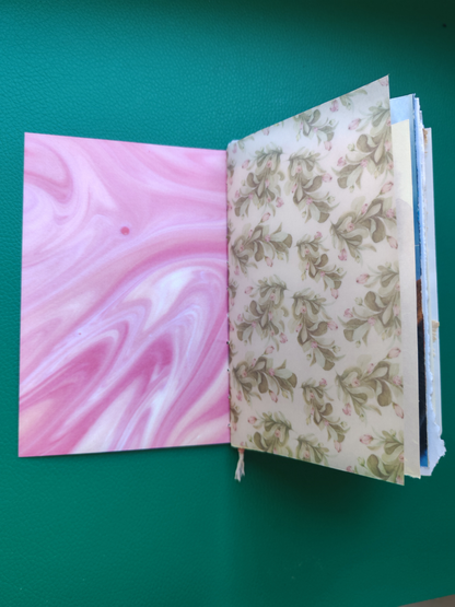 Open book with pink marbled page and floral patterned page on a green background