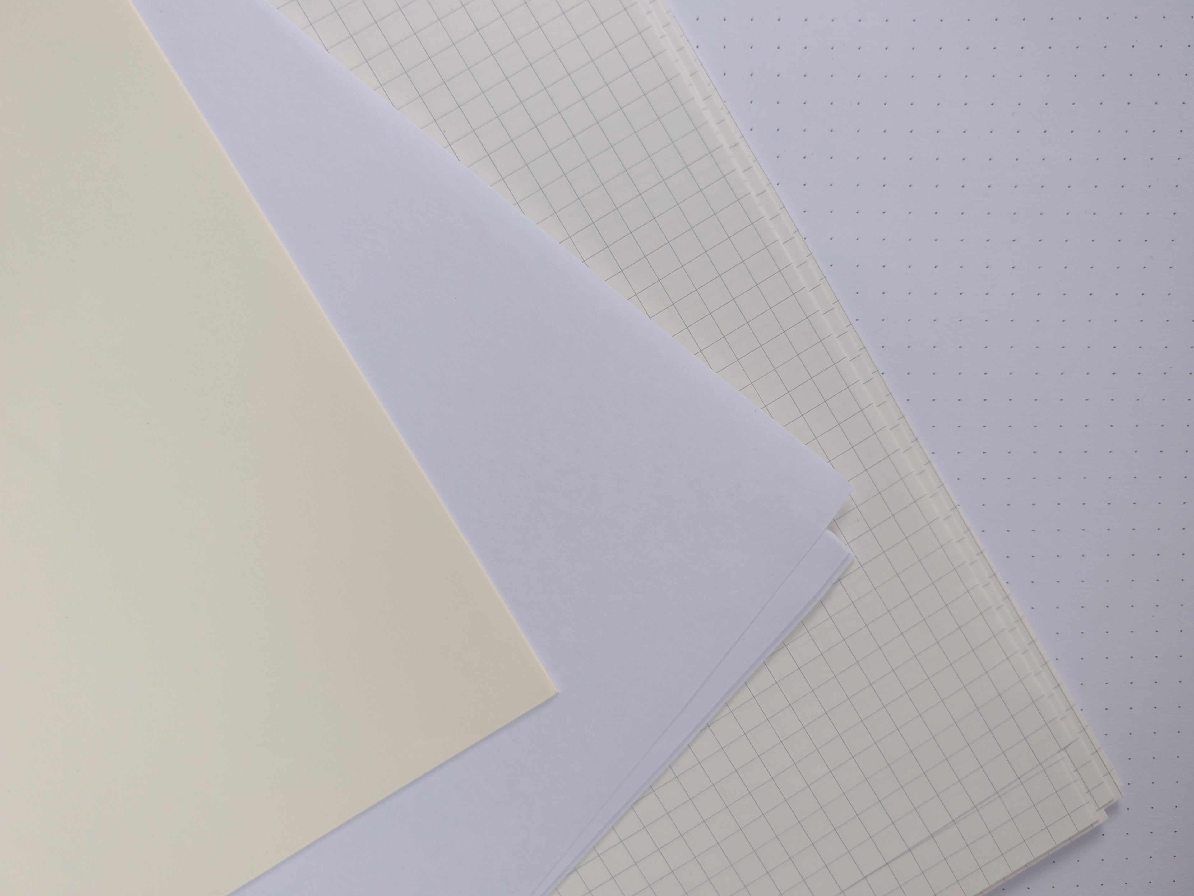 Collection of different types of paper including plain, grid, and colored sheets on a light gray background.