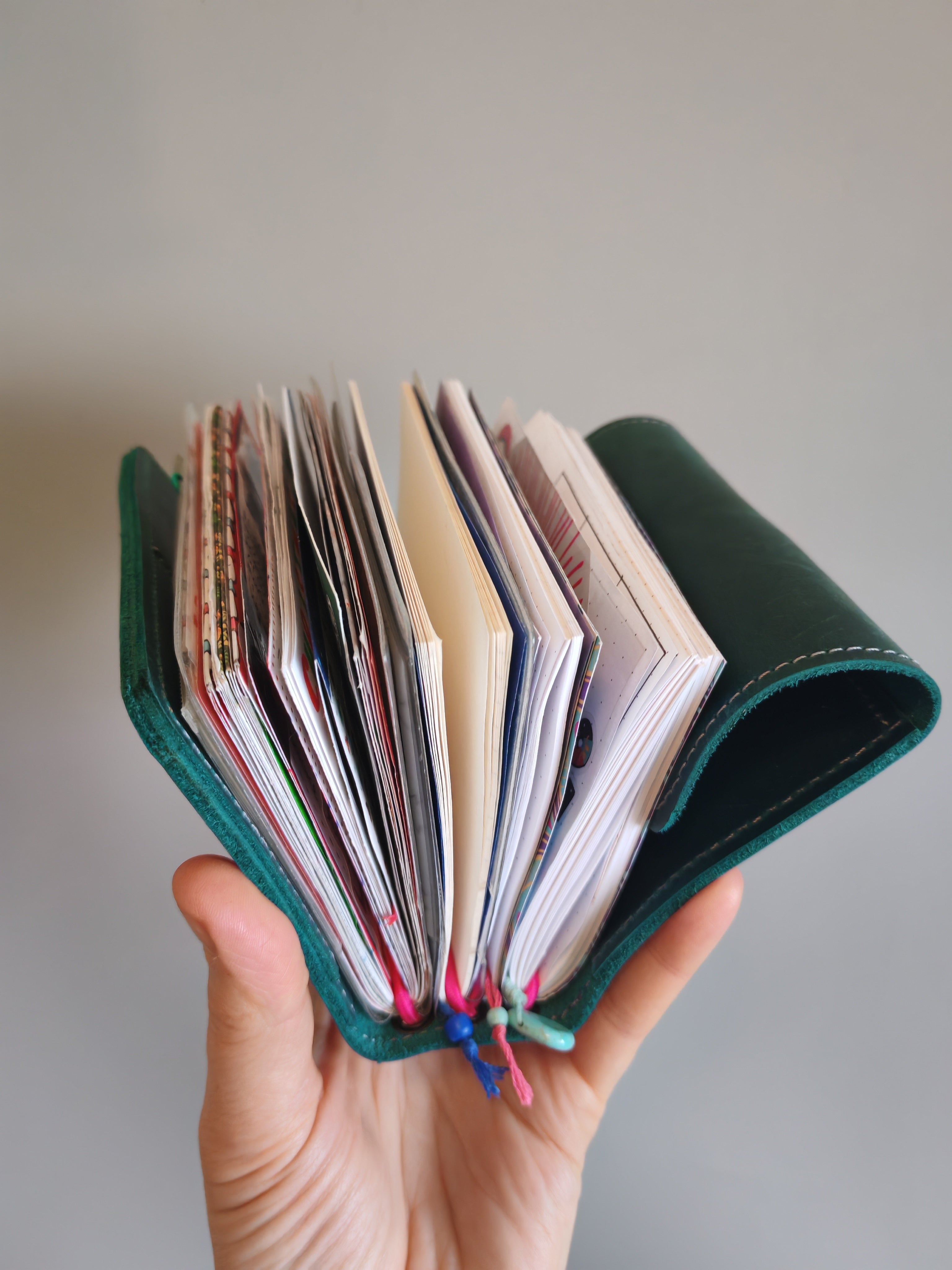 Hand holding a green leather-bound notebook cover spread open to reveal a selection of pocket notebooks within